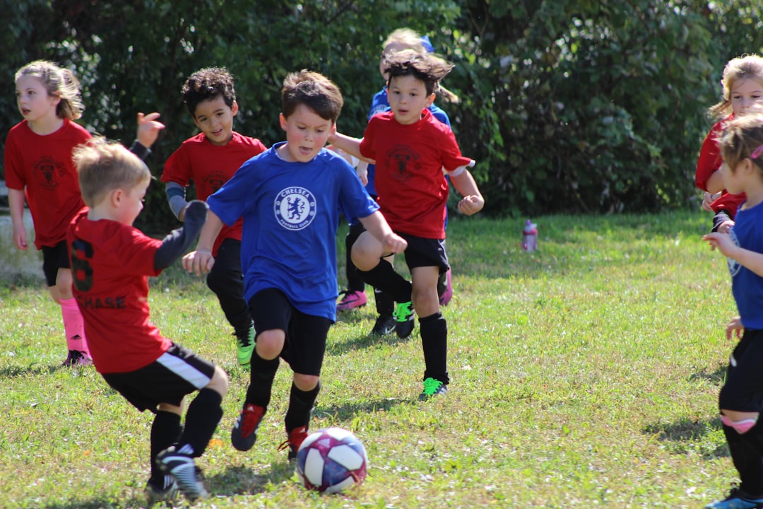 services-03 boy-in-red-and-blue-soccer-jersey-kicking-soccer-ball-on-green-grass-field-during-daytime-avgipreokfm