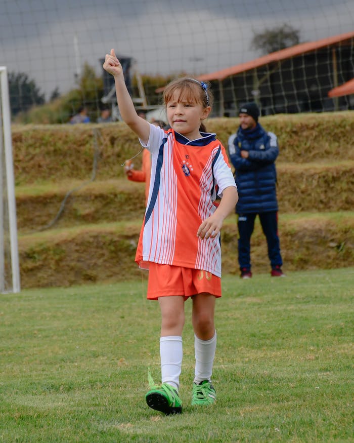 gallery-3 A young girl celebrates during a soccer match on a grassy field. Sport and childhood joy.