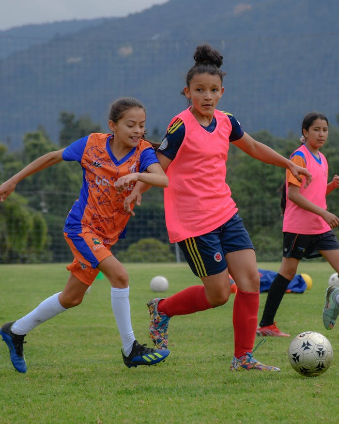 hero-img-02 Young girls enthusiastically playing soccer in a vibrant outdoor setting.