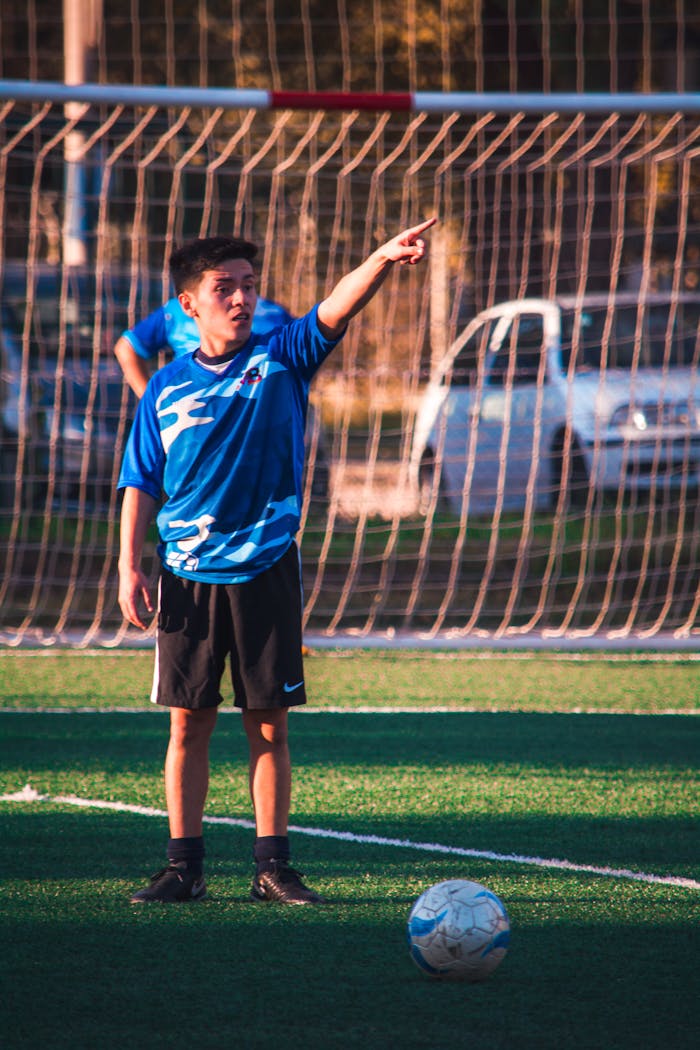 services-02 A teenage soccer player in blue jersey directing teammates during a game on a sunny day.